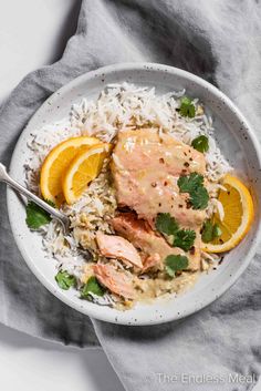 a white bowl filled with rice, oranges and salmon on top of a gray napkin