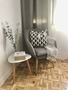 a living room with a chair, coffee table and vase on the floor in front of a window