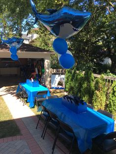 an outdoor party with blue table cloths and shark balloons