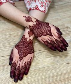 two hands with henna tattoos on them sitting on a wooden floor next to each other