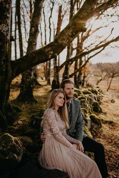 a man and woman sitting next to each other in front of some trees with moss