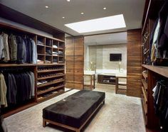 a large walk - in closet with lots of clothes on shelves and a footstool