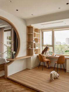 a woman sitting at a desk in front of a window with a dog on the floor