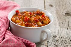 a white bowl filled with stew on top of a wooden table next to a red and white checkered napkin