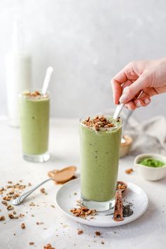 two glasses filled with green smoothie sitting on top of a white plate next to some spoons