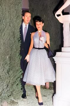 a man and woman standing next to each other in front of a tall green wall