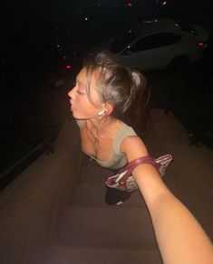 a woman sitting on the ground in front of a car at night with her hand up to her face