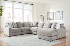 a living room with a large sectional couch and pillows on the floor in front of a window