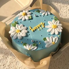 a blue cake decorated with white flowers and the words happy on it is in a box