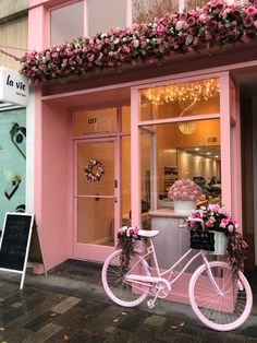 a pink bicycle is parked in front of a storefront with flowers on the windows