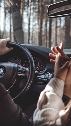 a person driving a car in the woods with their hands on the steering wheel and one hand on the dashboard