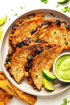 some tacos and guacamole on a white plate with lime wedges