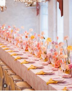 a long table is set with pink and yellow flowers in vases, candles and napkins