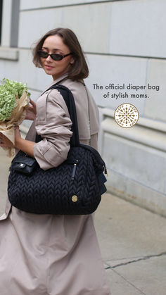 a woman walking down the street carrying a black purse and flowers in her hand,