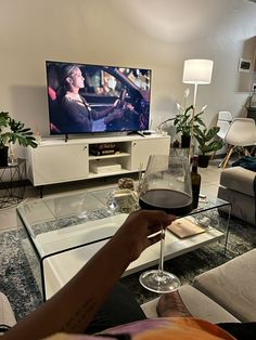 a person holding a glass of wine in front of a flat screen tv