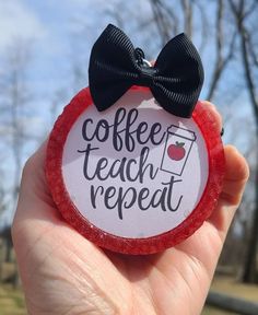 a person holding up a red lollipop with a black bow on it that says coffee teach repeat