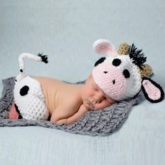 a baby wearing a cow hat laying on top of a blanket