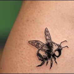 a small black and white bee tattoo on the back of a woman's shoulder