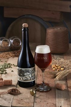 a bottle of beer next to a glass filled with liquid and grains on a wooden table