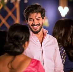 a man smiling while standing next to two other women in a room with lights on