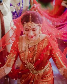 a woman in red and gold dress with veil on her head, smiling at the camera