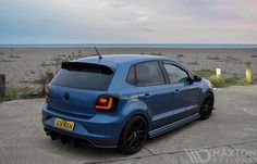 the rear end of a blue car parked on top of a parking lot next to an ocean