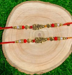 two red and gold beaded bracelets sitting on top of a tree stump in the grass