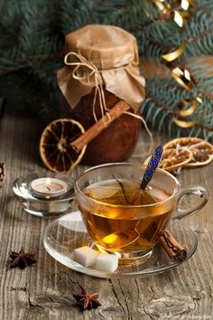 a glass cup filled with tea next to some cinnamons and an ornament