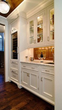 an elegant kitchen with white cabinets and wood flooring is seen in this image from the doorway to the dining room