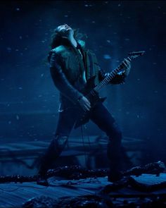 a man with long hair playing an electric guitar in the dark, while it's snowing