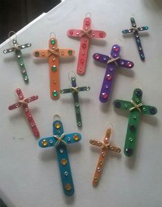 six colorful crosses are hanging on a white counter top, each decorated with colored beads