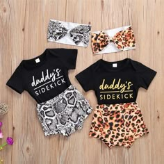 three baby girls'outfits with leopard print shorts and headbands on wooden surface