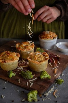 a person sprinkling cheese on top of mini quiche pies with broccoli