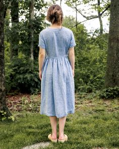 a woman is standing in the grass near some trees