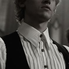 a young man with curly hair wearing a vest and striped shirt looking off to the side