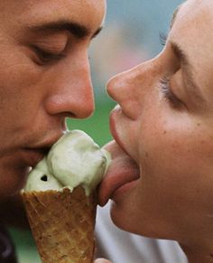 a man and woman kissing while eating an ice cream cone