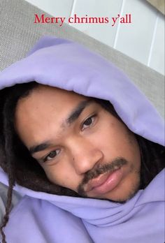 a man with dreadlocks and a purple hoodie is looking at the camera