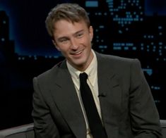 a smiling man in a suit and tie on the set of late show with jimmy stewart