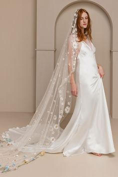 a woman in a white wedding dress with a veil over her head and flowers on the side