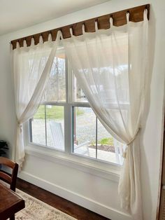 a window with white curtains and a wooden table in front of it, along with a rug on the floor