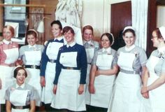 a group of women standing next to each other in front of a white wall holding papers