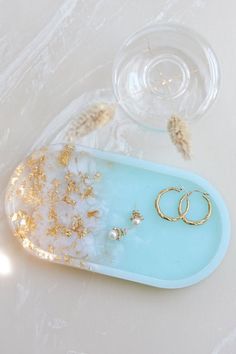 two gold wedding rings are sitting on a blue tray next to some seashells