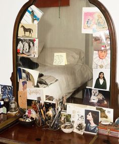 a mirror sitting on top of a wooden dresser filled with pictures and other items next to a bed