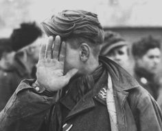 a black and white photo of a man covering his face with his hands while others look on