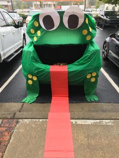 a large green frog sitting on top of a red carpet next to a parking lot