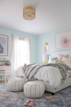 the bedroom is decorated in pastel colors and features an ottoman, bedding, and chandelier