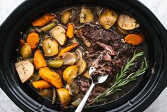 a crock pot filled with beef, potatoes and carrots next to a spoon