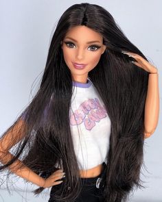 a barbie doll with long black hair wearing a white shirt and black pants, posing for the camera