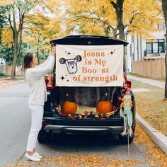 a woman placing a sign on the back of a car that says jesus is my boo st of strength