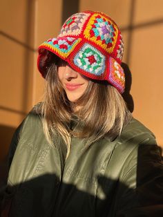 a woman wearing a colorful crocheted hat while looking at her cell phone in the sun